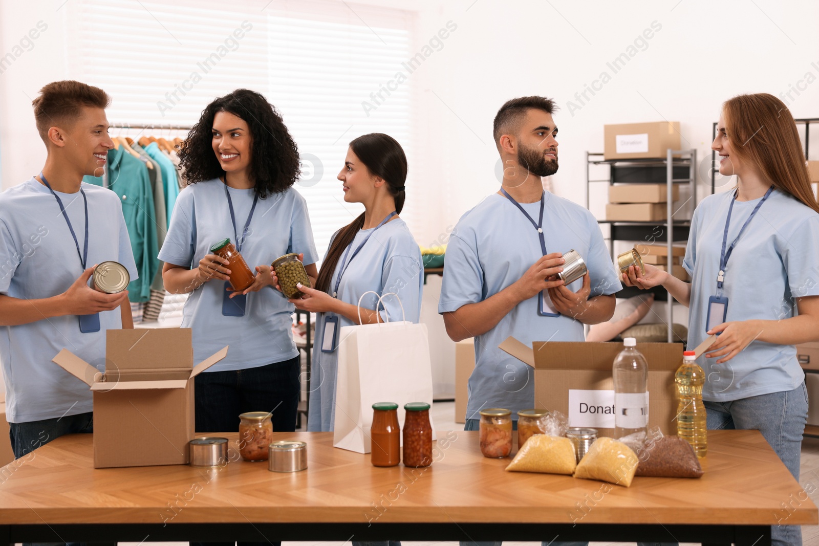 Photo of Group of volunteers packing food products at table in warehouse