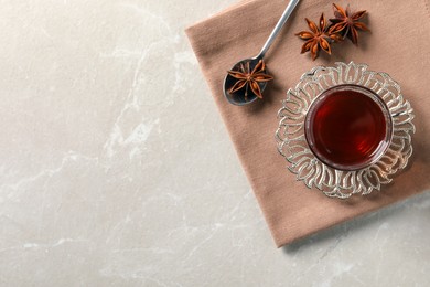 Photo of Glass of traditional Turkish tea in vintage holder and anise stars on white marble table, top view. Space for text