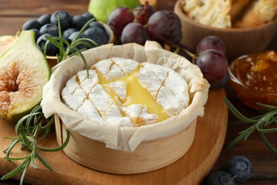 Photo of Tasty baked brie cheese and products on wooden table, closeup
