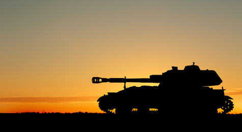 Image of Silhouette of army tank at sunset outdoors. Military machinery