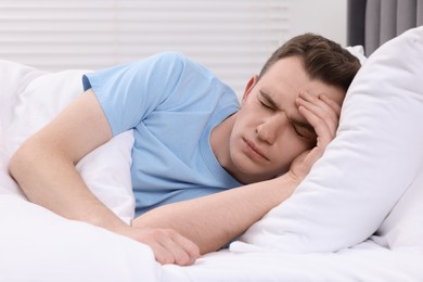 Photo of Sad man suffering from headache in bed indoors