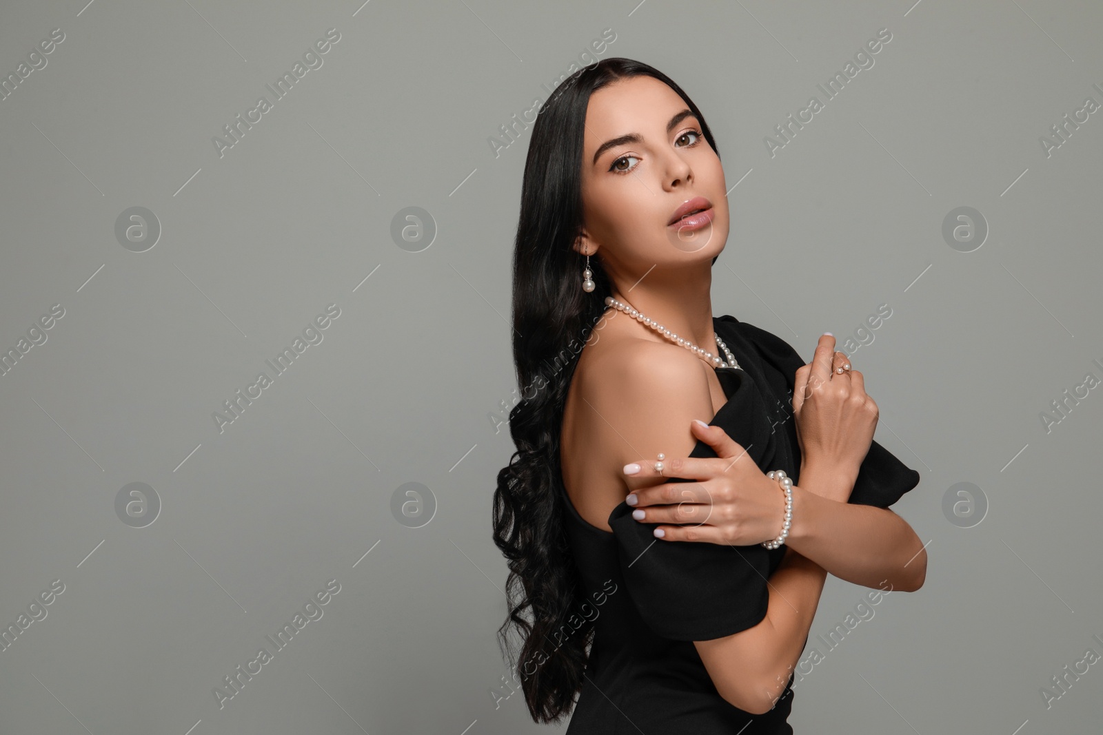 Photo of Young woman wearing elegant pearl jewelry on grey background, space for text