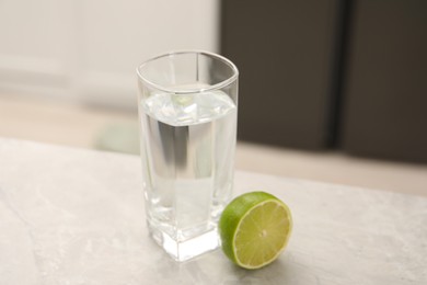 Photo of Filtered water in glass and lime on light table in kitchen, closeup