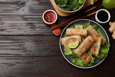 Photo of Tasty fried spring rolls, lettuce, sauce and lime on wooden table, flat lay. Space for text