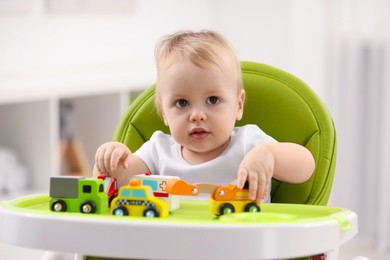 Photo of Children toys. Cute little boy playing with toy cars in high chair at home