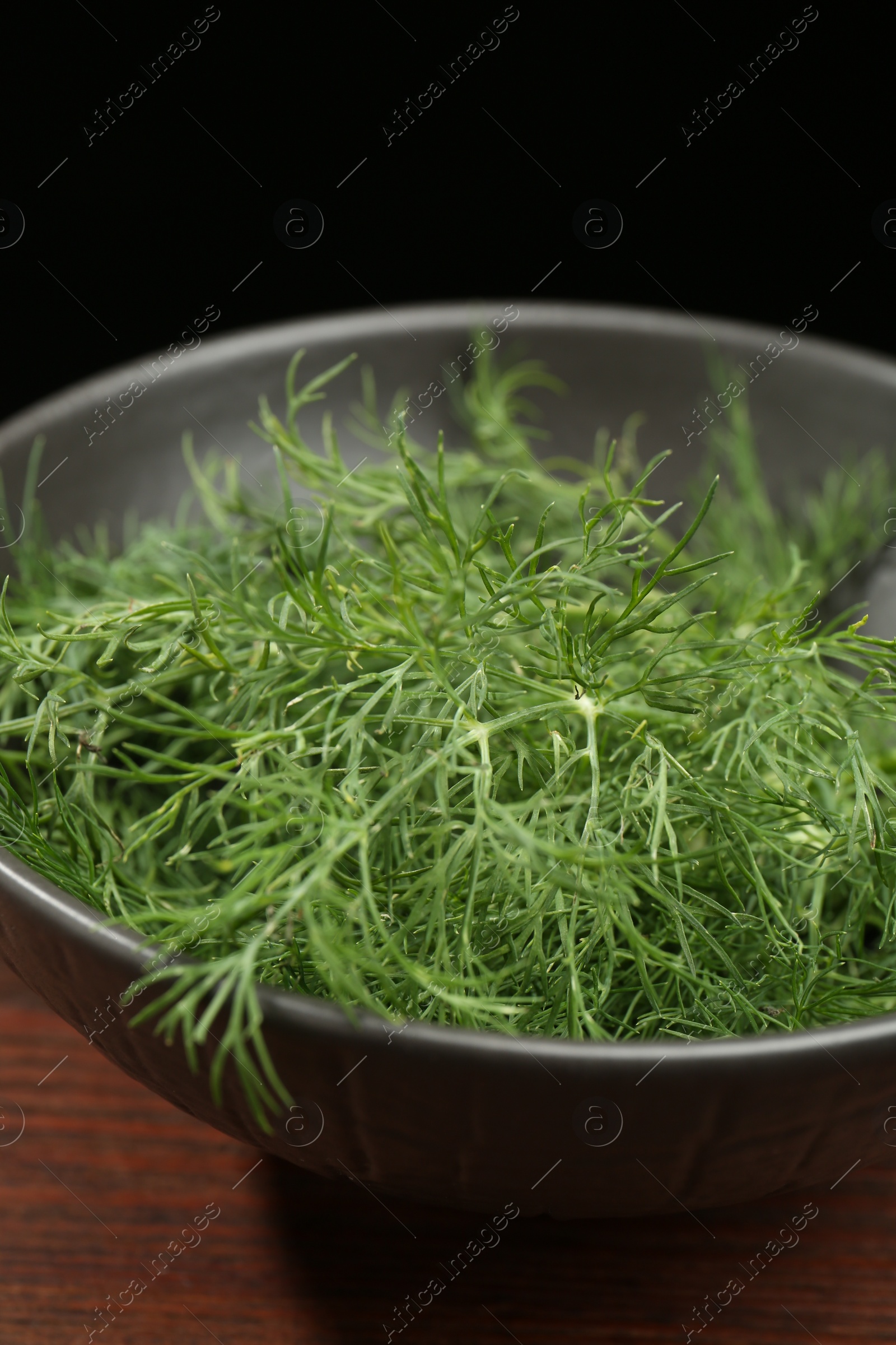 Photo of Bowl of fresh green dill on wooden table against black background, closeup