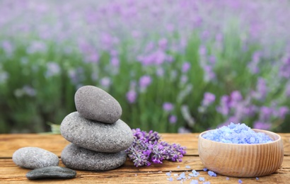 Spa stones, fresh lavender flowers and bath salt on wooden table outdoors, closeup