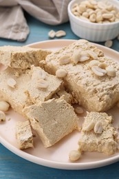 Photo of Pieces of tasty halva and peanuts on light blue table, closeup