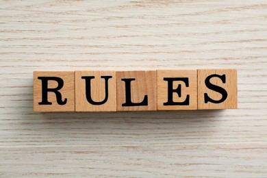 Photo of Word Rules made of cubes with letters on light wooden table, top view