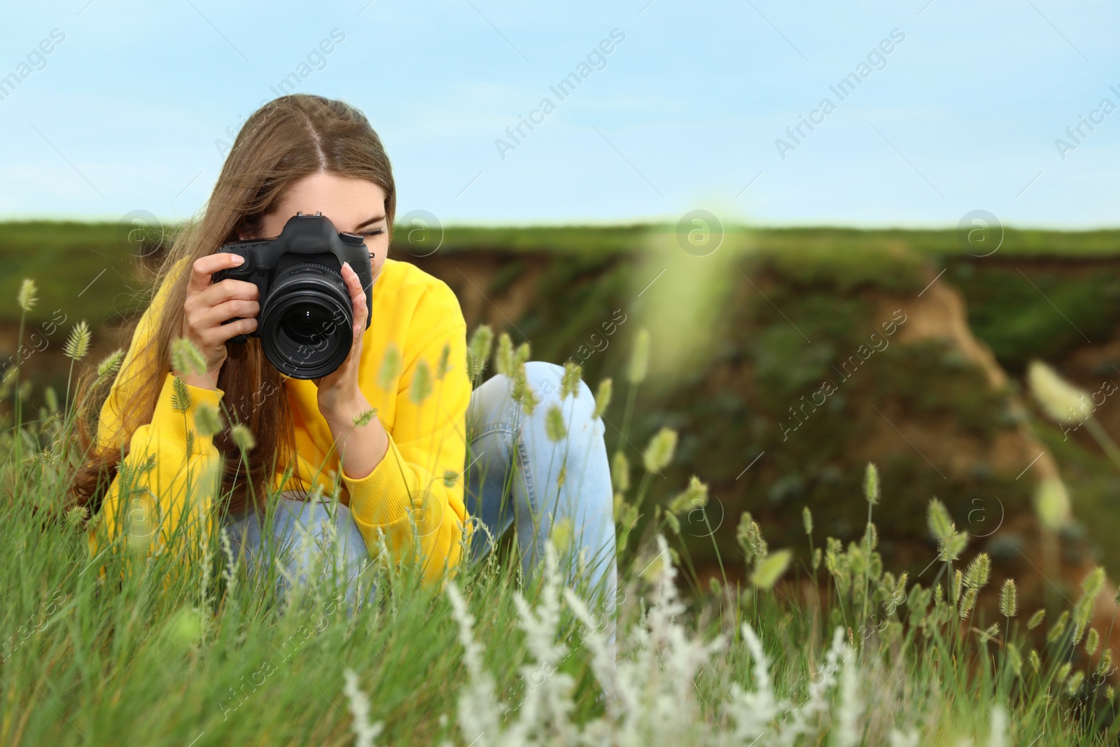 Photo of Female photographer taking picture of beautiful plants with professional camera on green hill