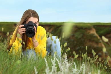Photo of Female photographer taking picture of beautiful plants with professional camera on green hill