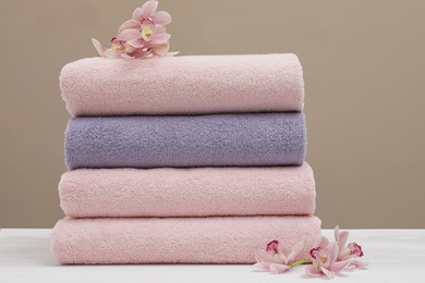 Photo of Stack of fresh towels with flowers on table