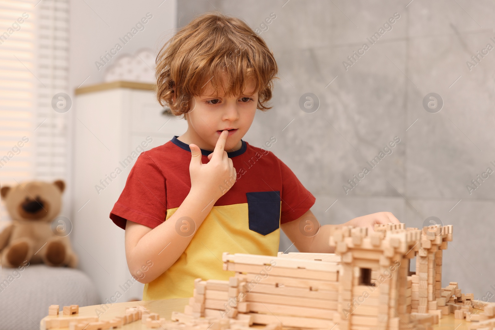 Photo of Cute little boy playing with wooden construction set at table in room. Child's toy