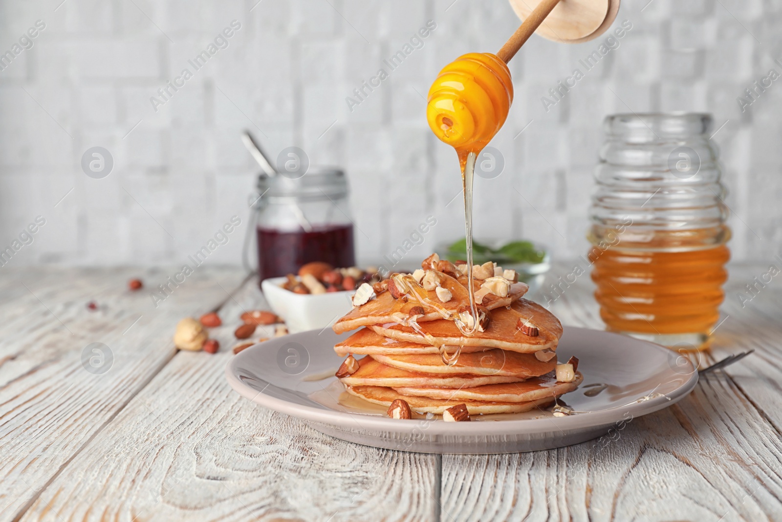 Photo of Pouring honey on stack of tasty pancakes on wooden table