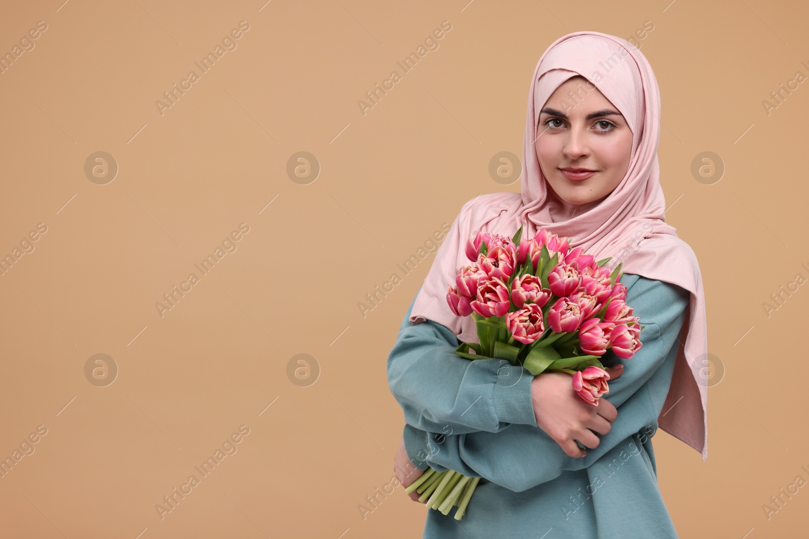 Photo of Happy woman in hijab with beautiful bouquet on beige background. Space for text