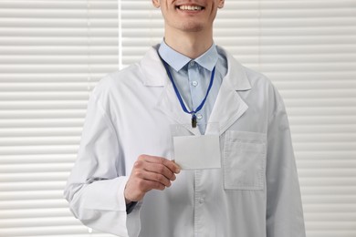 Photo of Smiling doctor showing empty badge in hospital, closeup