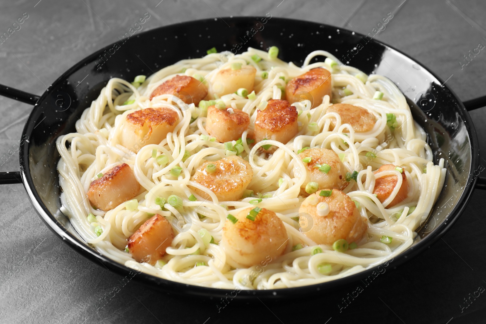 Photo of Delicious scallop pasta with green onion on grey table