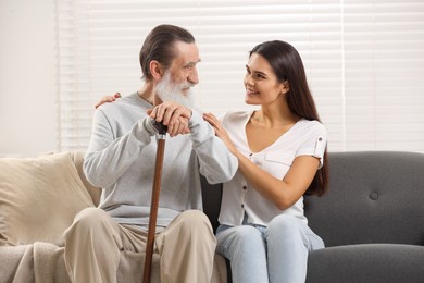 Photo of Senior man with walking cane and young woman on sofa at home