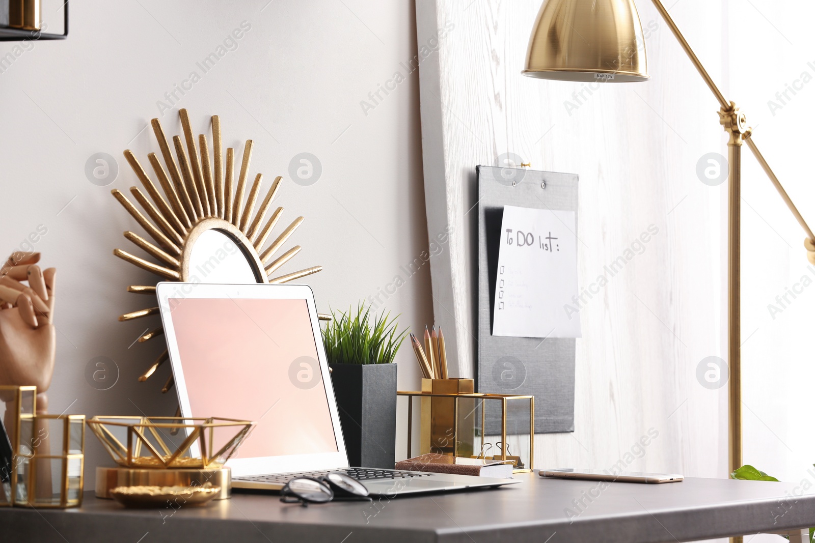 Photo of Modern workplace with laptop and golden decor on desk near wall. Stylish interior design