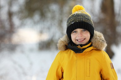 Photo of Cute little boy in snowy park on winter day, space for text