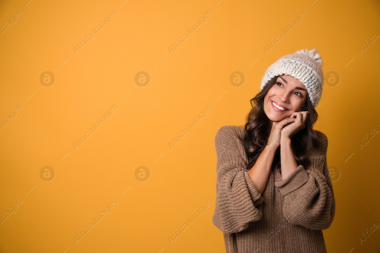 Photo of Young woman in warm sweater and hat on yellow background, space for text. Christmas season