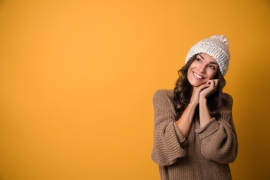 Young woman in warm sweater and hat on yellow background, space for text. Christmas season