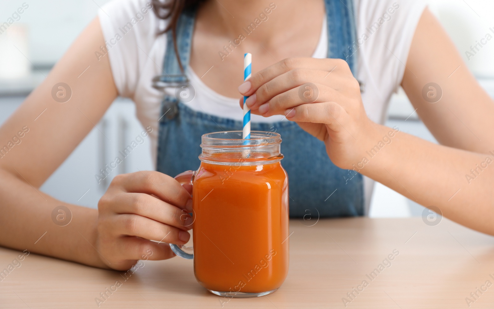 Photo of Woman with mason jar of tasty carrot juice at table indoors, closeup