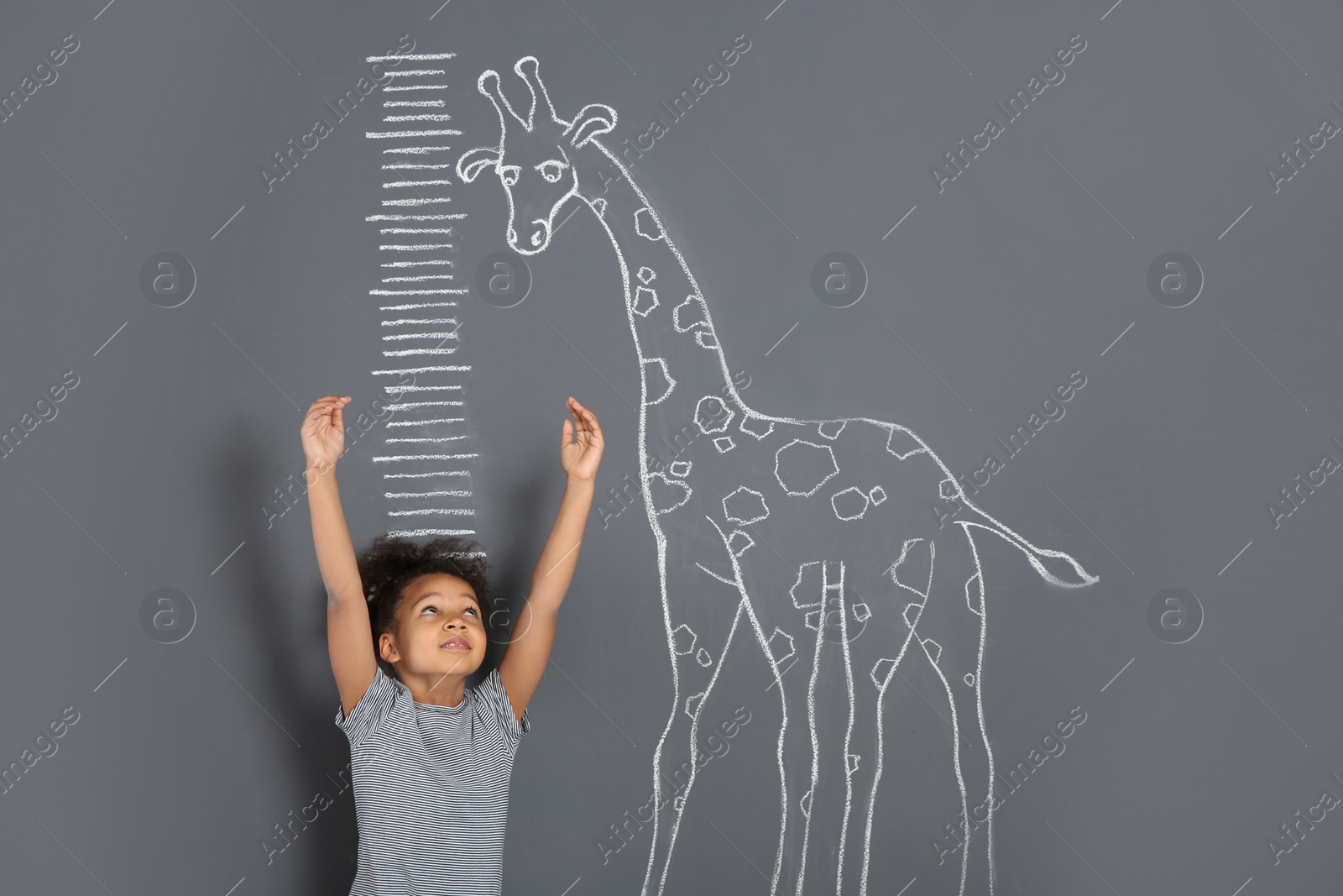 Photo of African-American child measuring height near chalk giraffe drawing on grey background