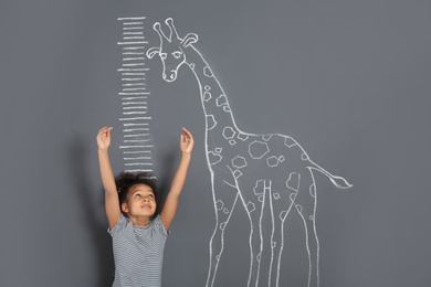 African-American child measuring height near chalk giraffe drawing on grey background