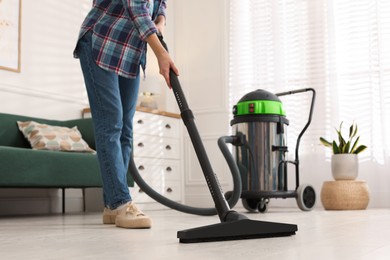Photo of Woman vacuuming floor in living room, closeup