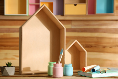 Photo of Composition with house shaped shelves and jars of paints on wooden table. Interior elements