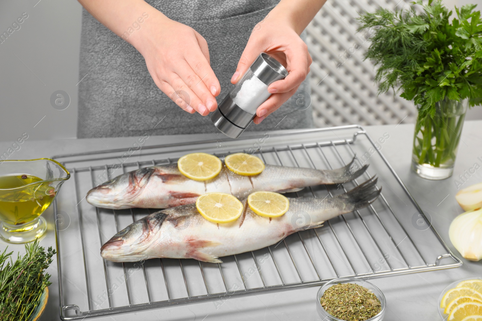 Photo of Woman salting raw sea bass fish with lemon at table, closeup