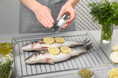Woman salting raw sea bass fish with lemon at table, closeup