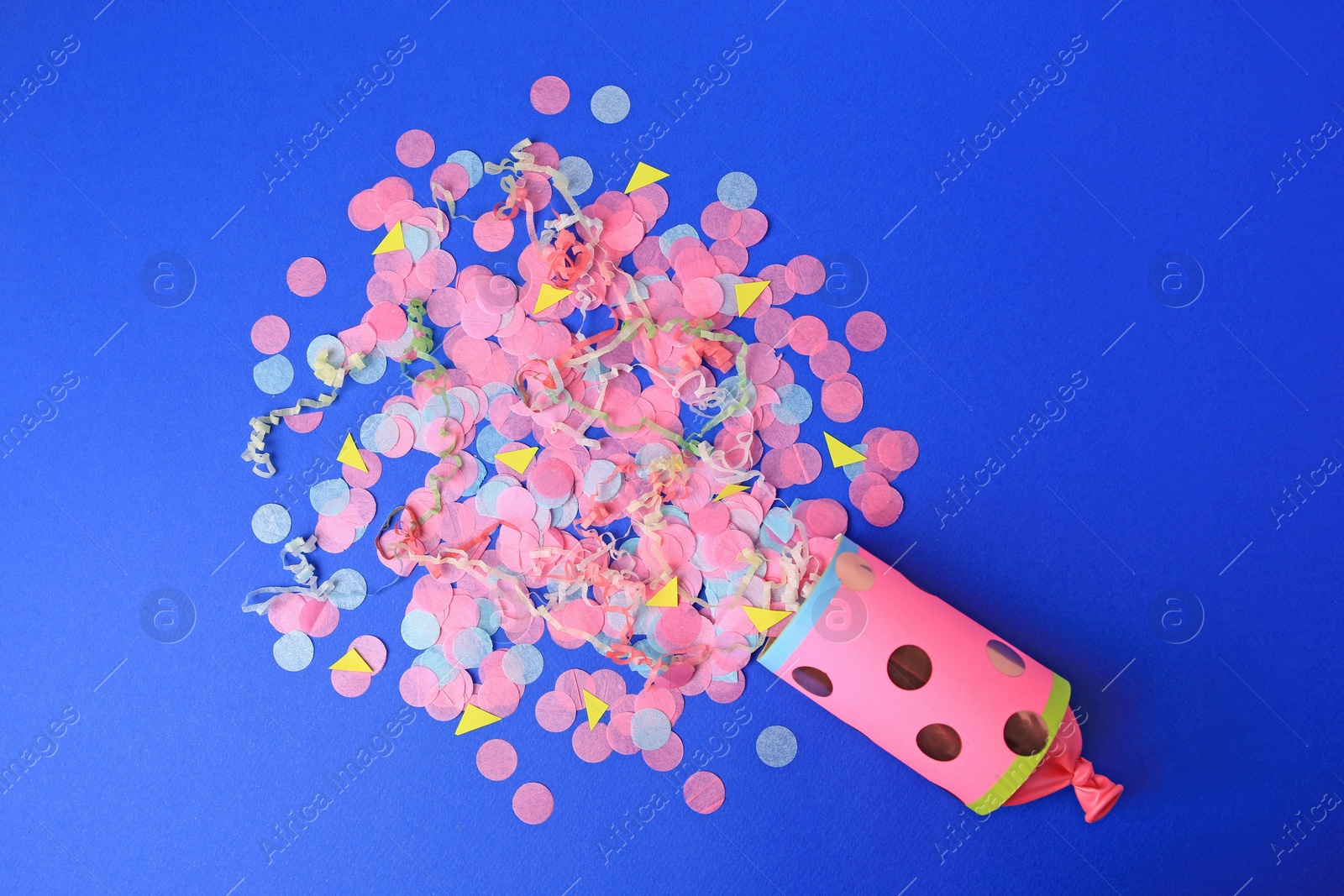 Photo of Colorful confetti and streamers bursting out of party cracker on blue background, flat lay