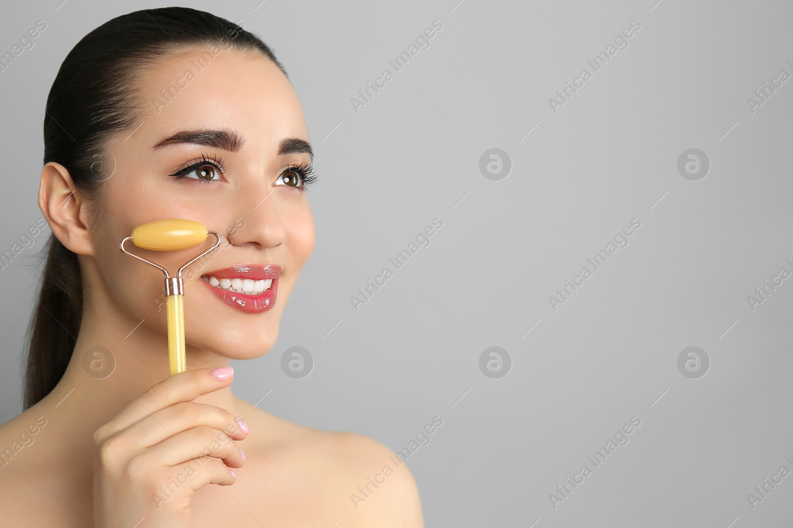 Photo of Woman using natural jade face roller on grey background, space for text