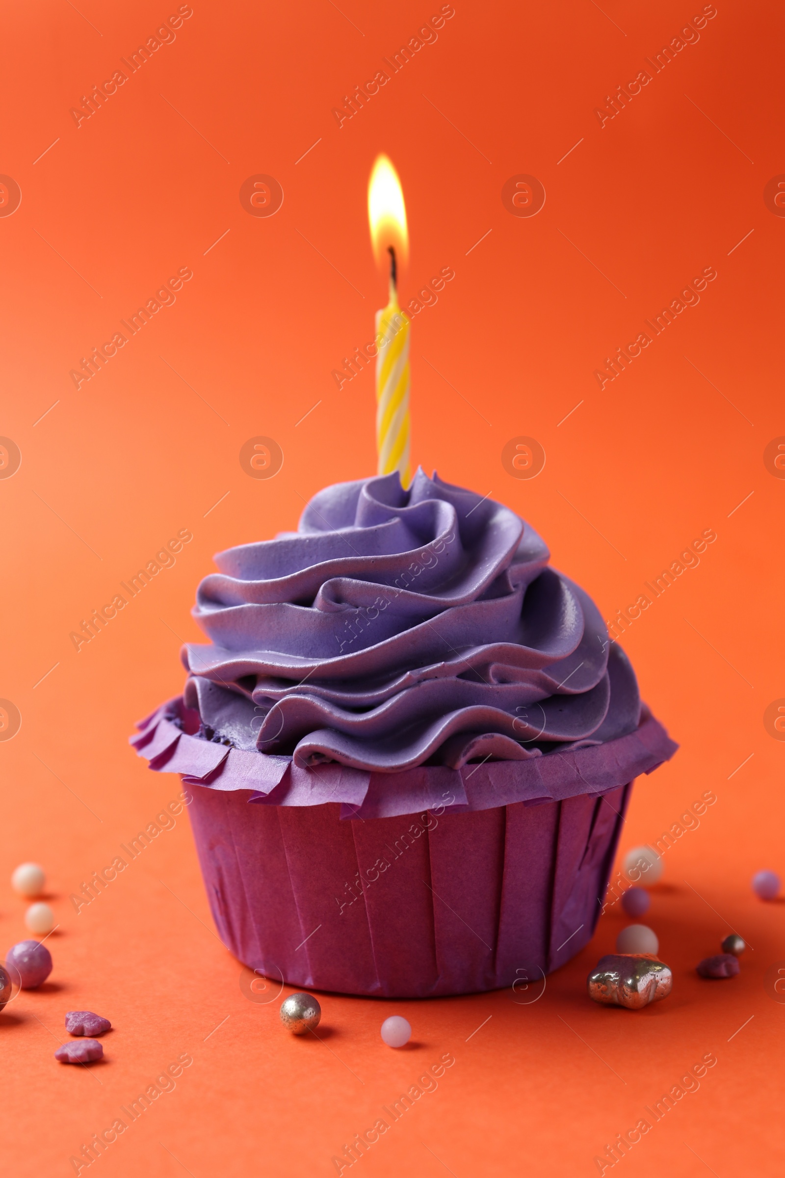 Photo of Delicious birthday cupcake with burning candle and sprinkles on coral background, closeup