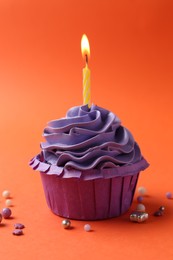 Photo of Delicious birthday cupcake with burning candle and sprinkles on coral background, closeup