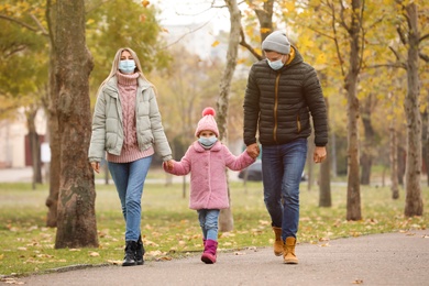 Family in medical masks walking outdoors on autumn day. Protective measures during coronavirus quarantine