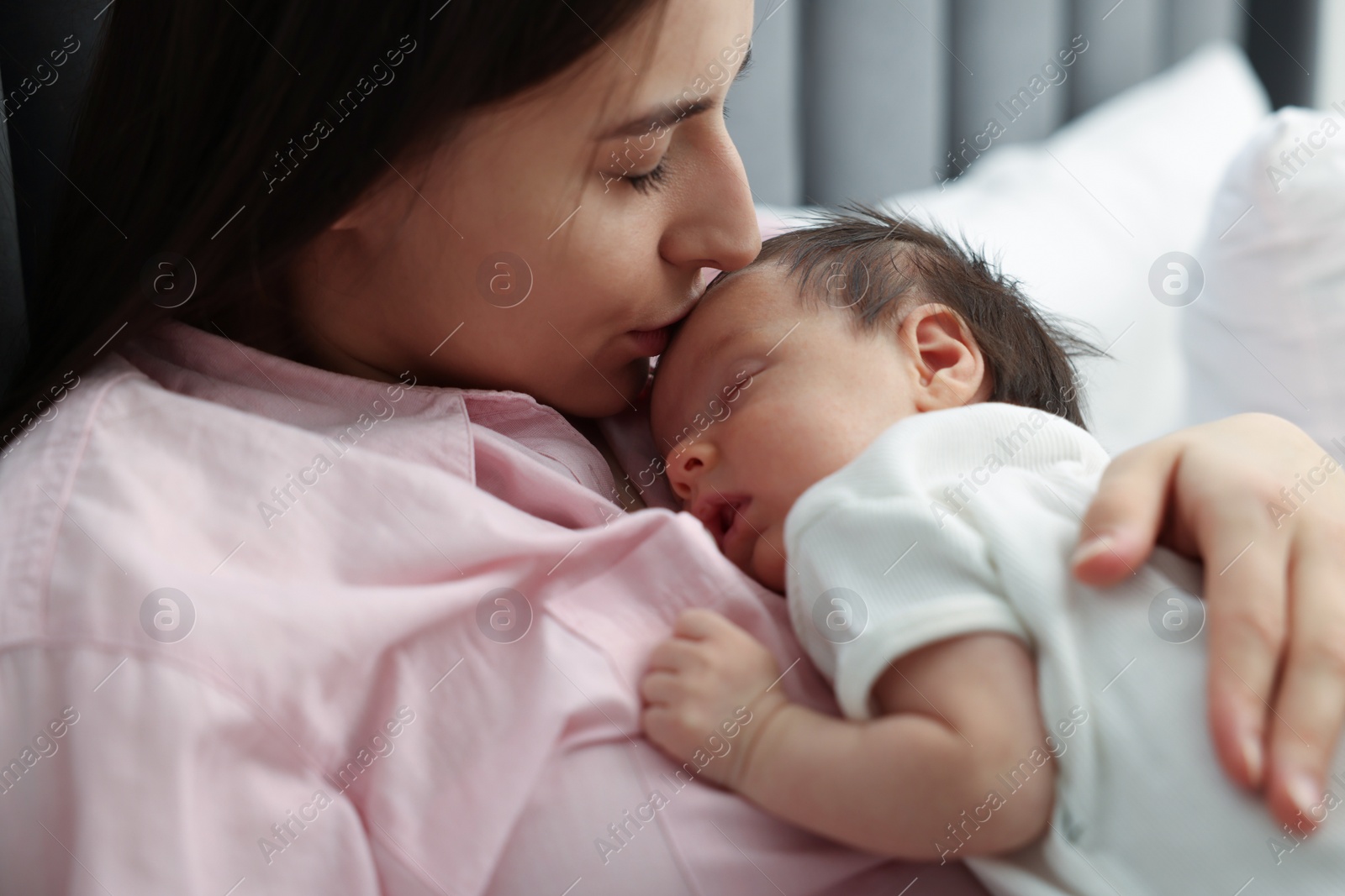 Photo of Mother kissing her sleeping newborn baby in bed