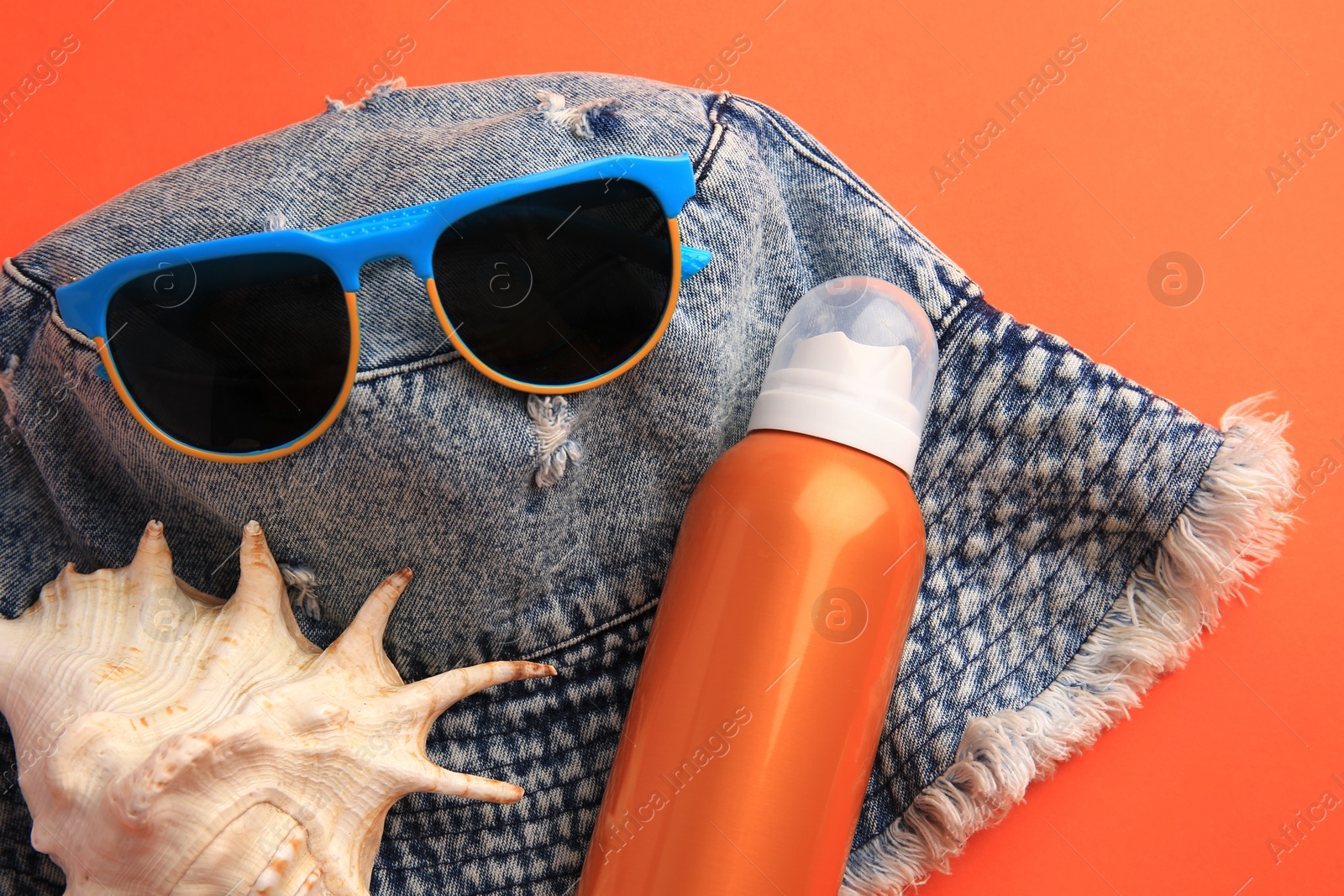 Photo of Bottle of sunscreen, seashell and beach accessories on coral background, flat lay
