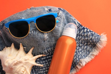 Bottle of sunscreen, seashell and beach accessories on coral background, flat lay