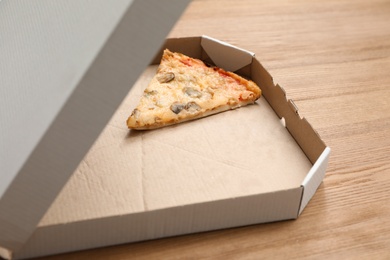 Cardboard box with pizza piece on wooden table