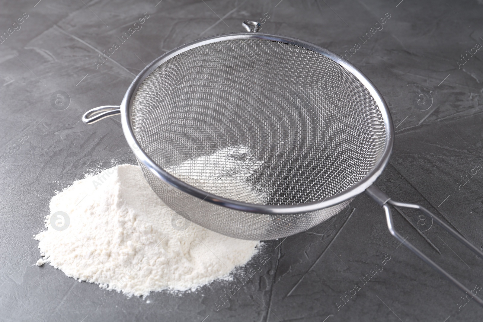 Photo of Metal sieve and flour on grey table, closeup