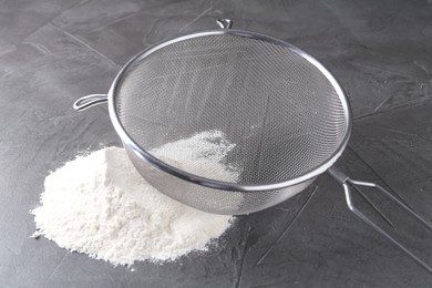 Metal sieve and flour on grey table, closeup