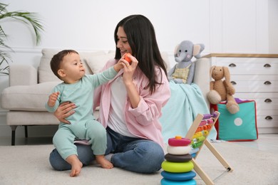 Cute baby boy playing with mother and toys on floor at home