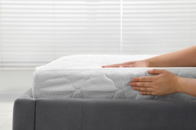 Photo of Woman touching soft light green mattress indoors, closeup