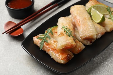 Tasty fried spring rolls, arugula, lime and sauce on grey textured table, closeup