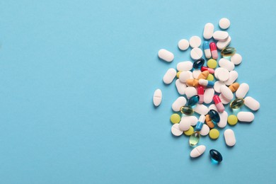 Pile of different pills on light blue background, flat lay. Space for text