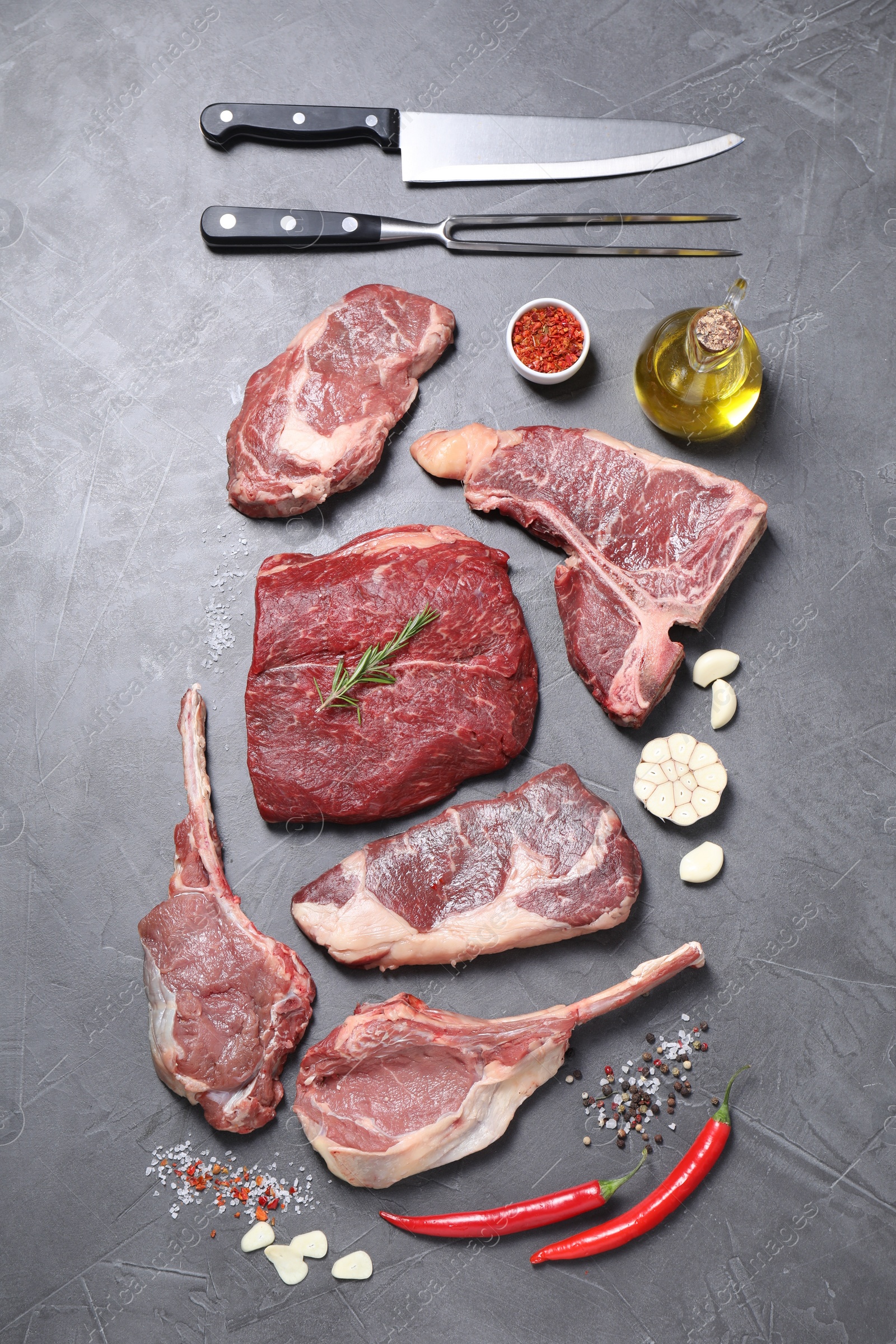 Photo of Fresh raw beef cuts, spices and butcher tools on light grey textured table, flat lay