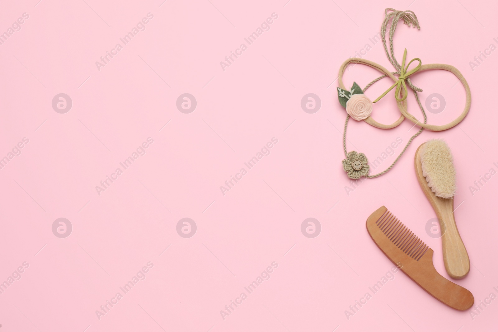 Photo of Baby wooden hairbrush, comb and headbands on light pink background, flat lay. Space for text